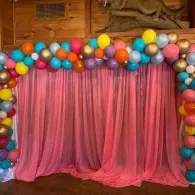 Pink curtain backdrop framed by colorful balloons in a festive indoor setting