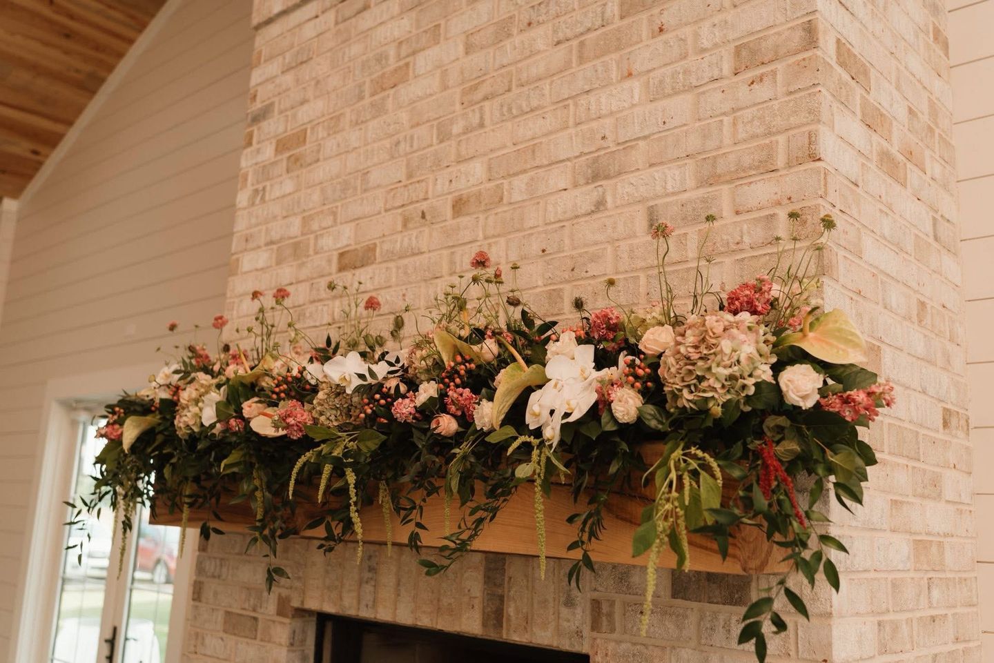 Flower arrangement on a fireplace mantel against a light brick wall