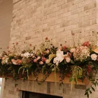 Floral arrangement of white, pink, and red flowers across a brick fireplace mantel