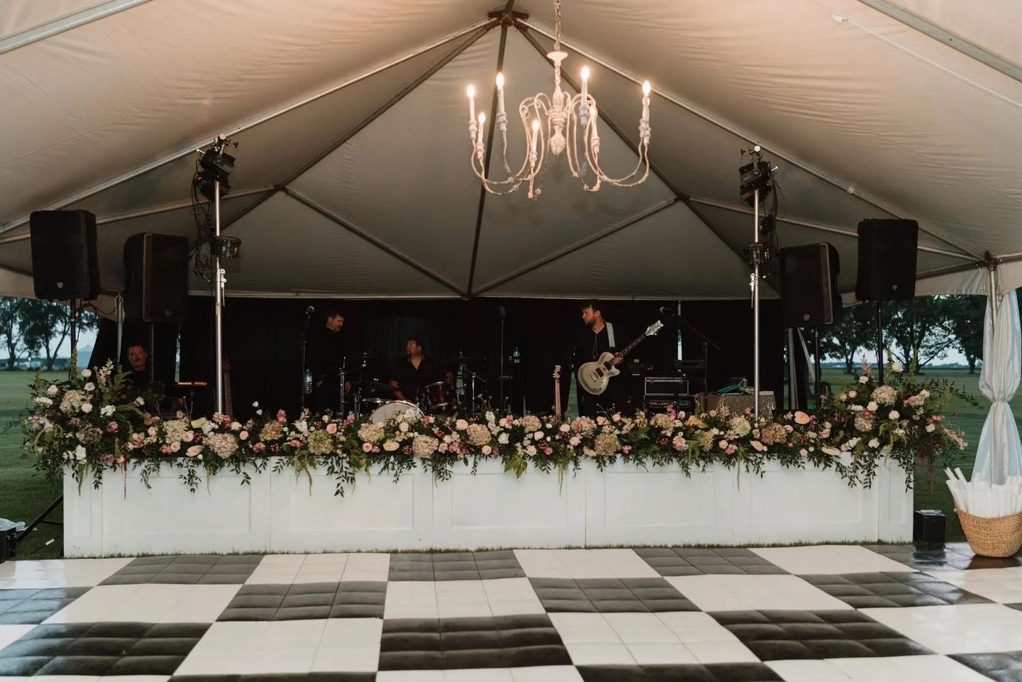 Elegant outdoor wedding reception tent with chandelier, floral stage, and black-and-white checkered floor