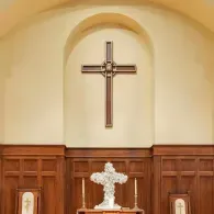 Church altar with a large cross on a cream wall and wood-paneled backdrop