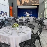 Banquet hall with round tables, black chairs, and a blue stage backdrop for an event