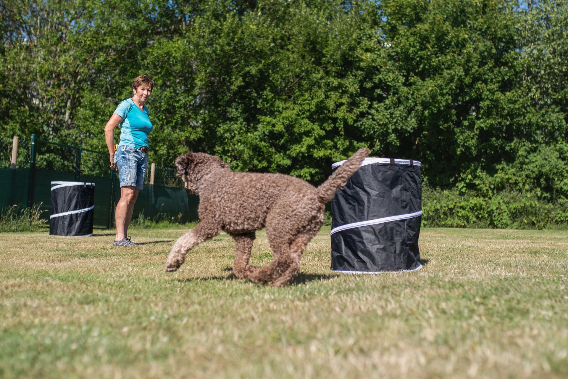 Frau mit ihrem Hund im Hoopers Parcours, Hund rennt um eine Hoopers Tonne