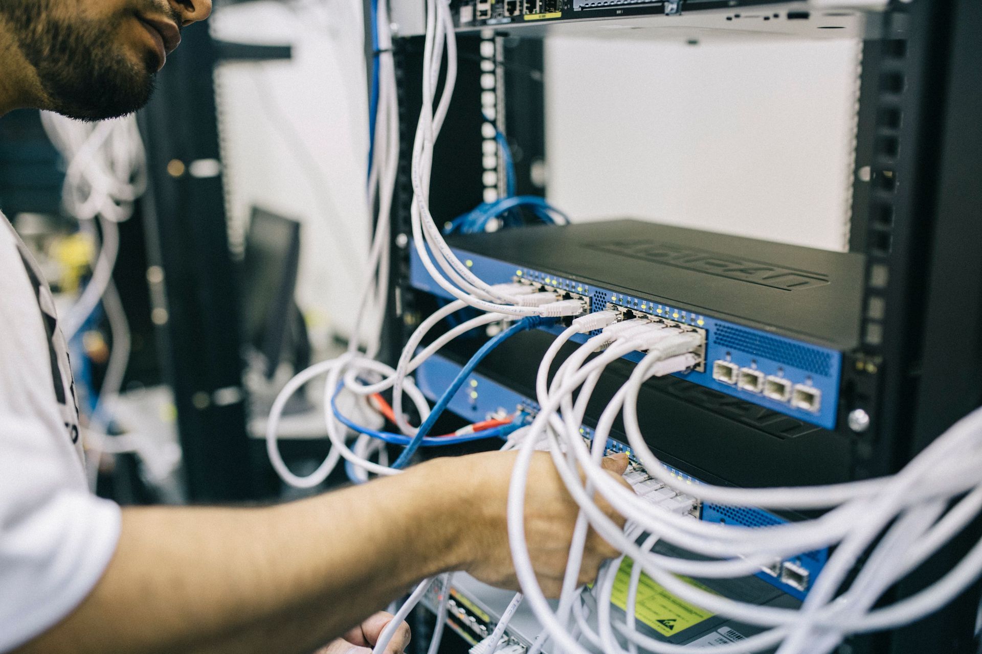 Technician connecting network cables to a blue switch in a server rack