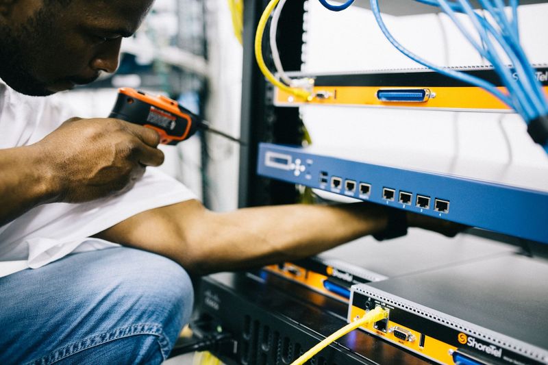 Technician using a handheld tester on network equipment with cables in a server rack