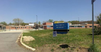 Blue school sign in front of a low brick campus building on a sunny day Blue school sign in front of a low brick campus building on a sunny day