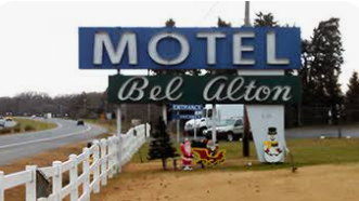 Motel sign reading “MOTEL Bel-Aton” beside a roadside with white fence and small display figures