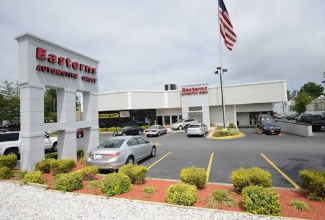 Car dealership lot with a white building, parked cars, and an Eastern sign under a cloudy sky