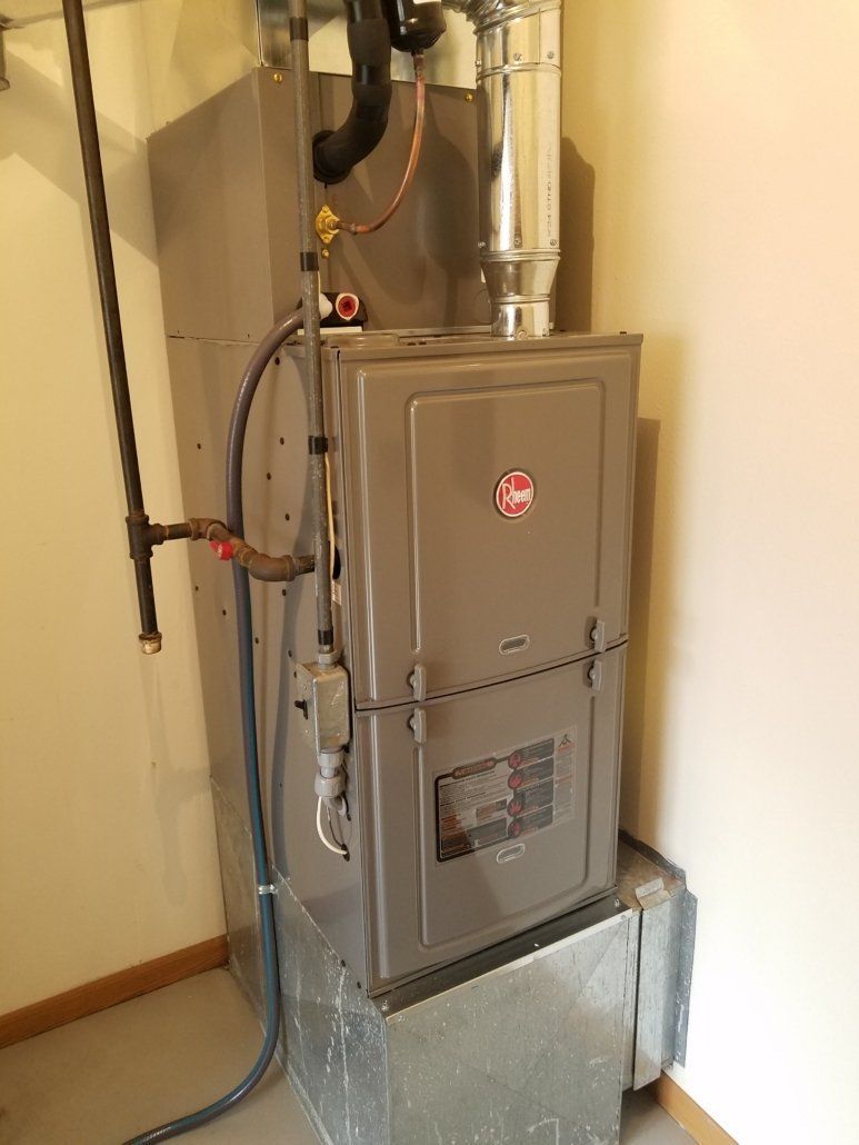Gas furnace in a basement utility area with exposed pipes and ductwork.