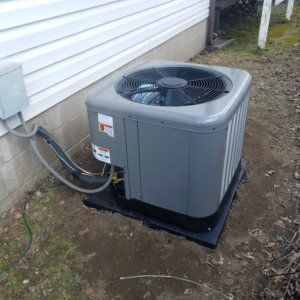 Outdoor gray air conditioner unit beside a house on a black pad