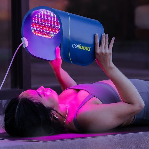 Woman using a blue Celluma LED light device on her chest outdoors.