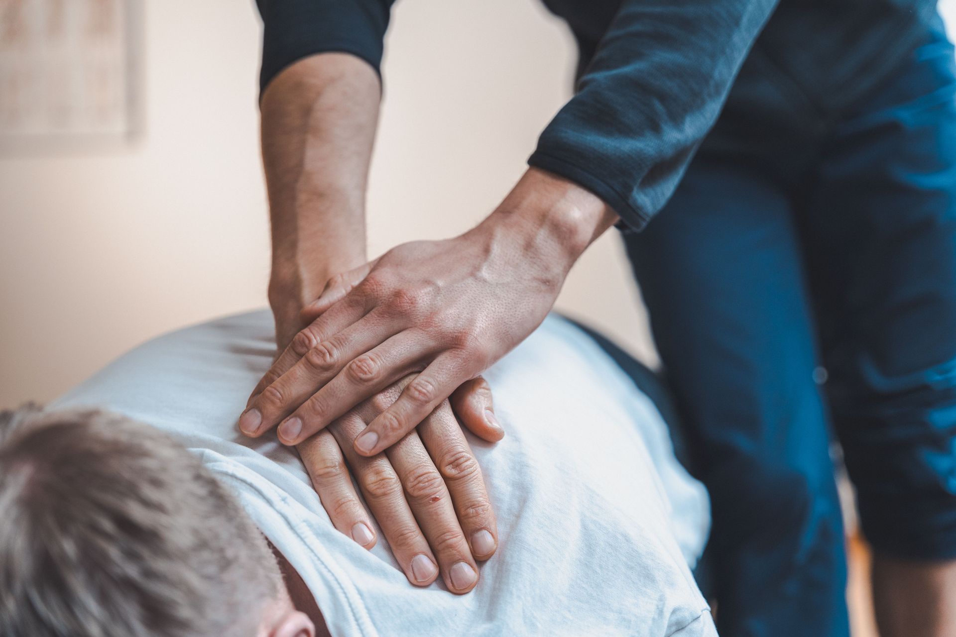 Hands on a person's back, likely for a chiropractic adjustment, indoors.