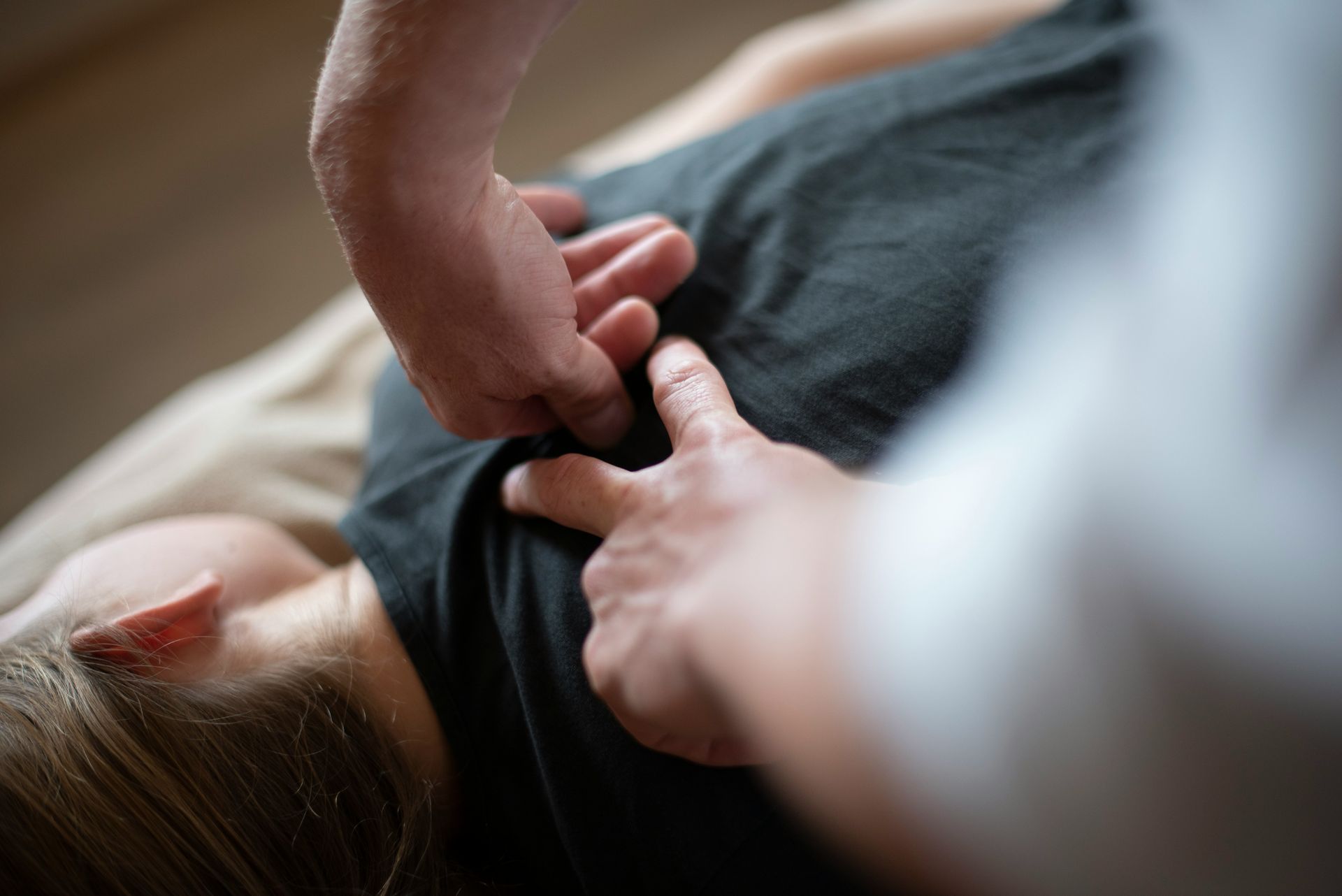 Hands pressing on a person's back, likely during a chiropractic examination or massage; soft focus.