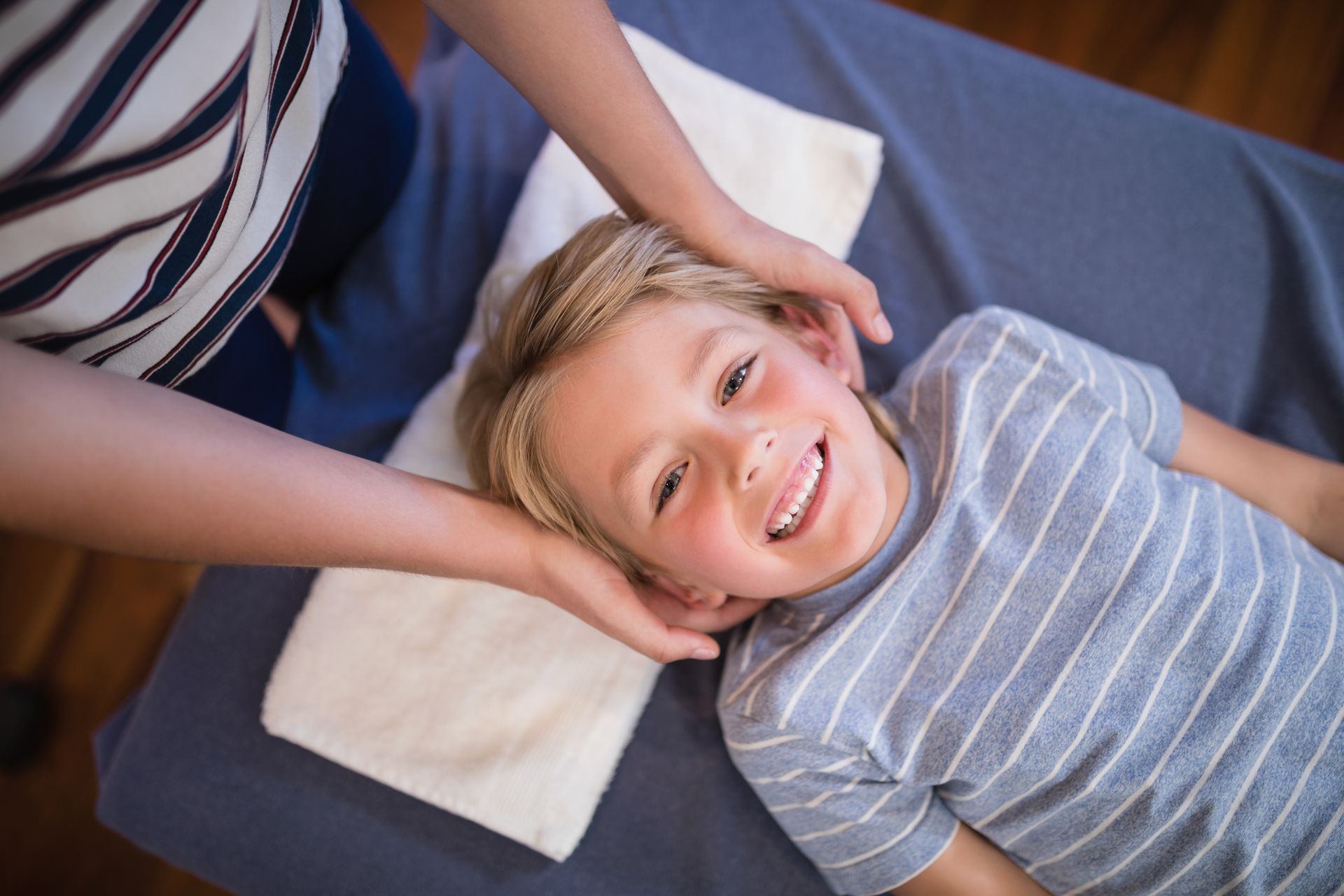 Boy smiling as hands gently cradle his head on a treatment table with a white pillow.