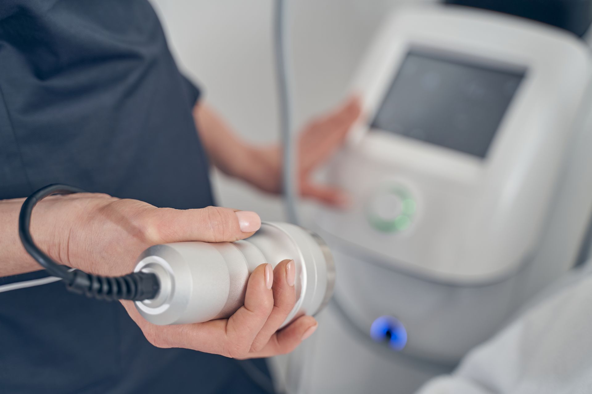 Person holding a radial shockwave device, with a machine in the background.