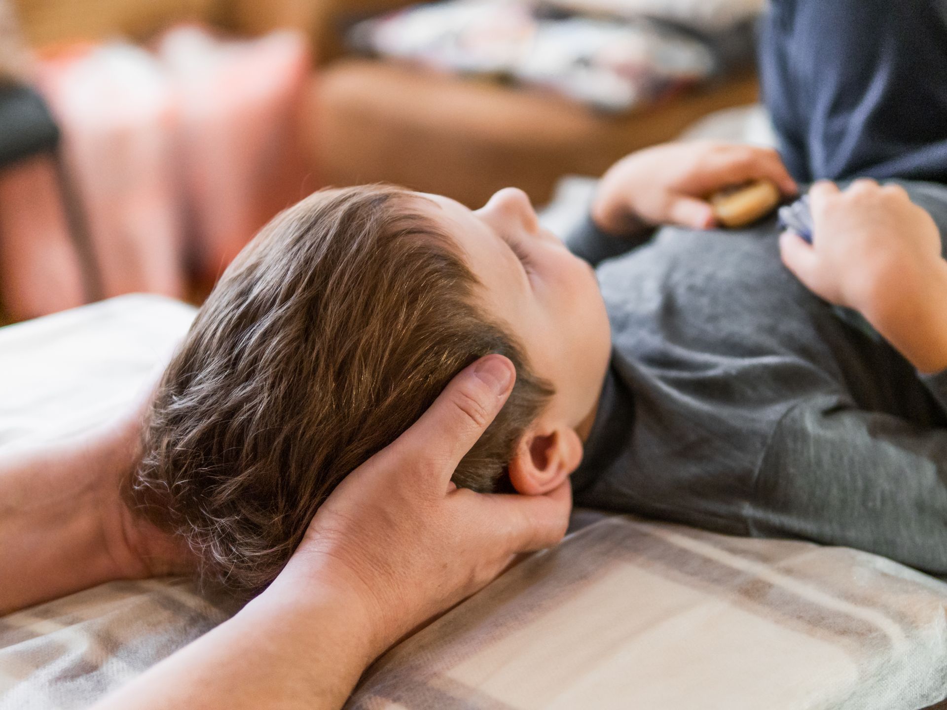 Hands gently supporting a child's head. The child lies on a blanket, eyes closed.