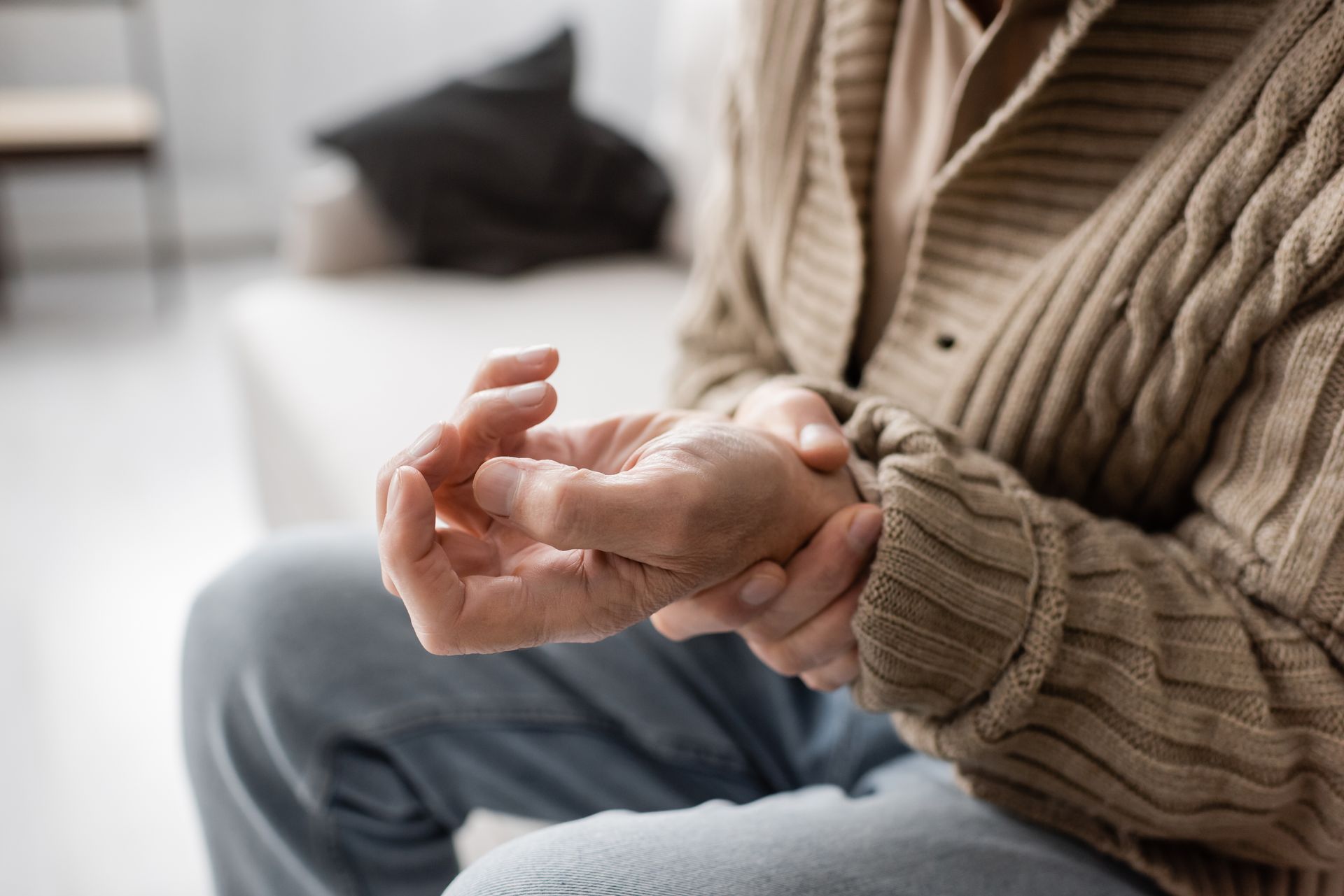 Person holding their wrist, showing discomfort. They are wearing a sweater and jeans, indoors.