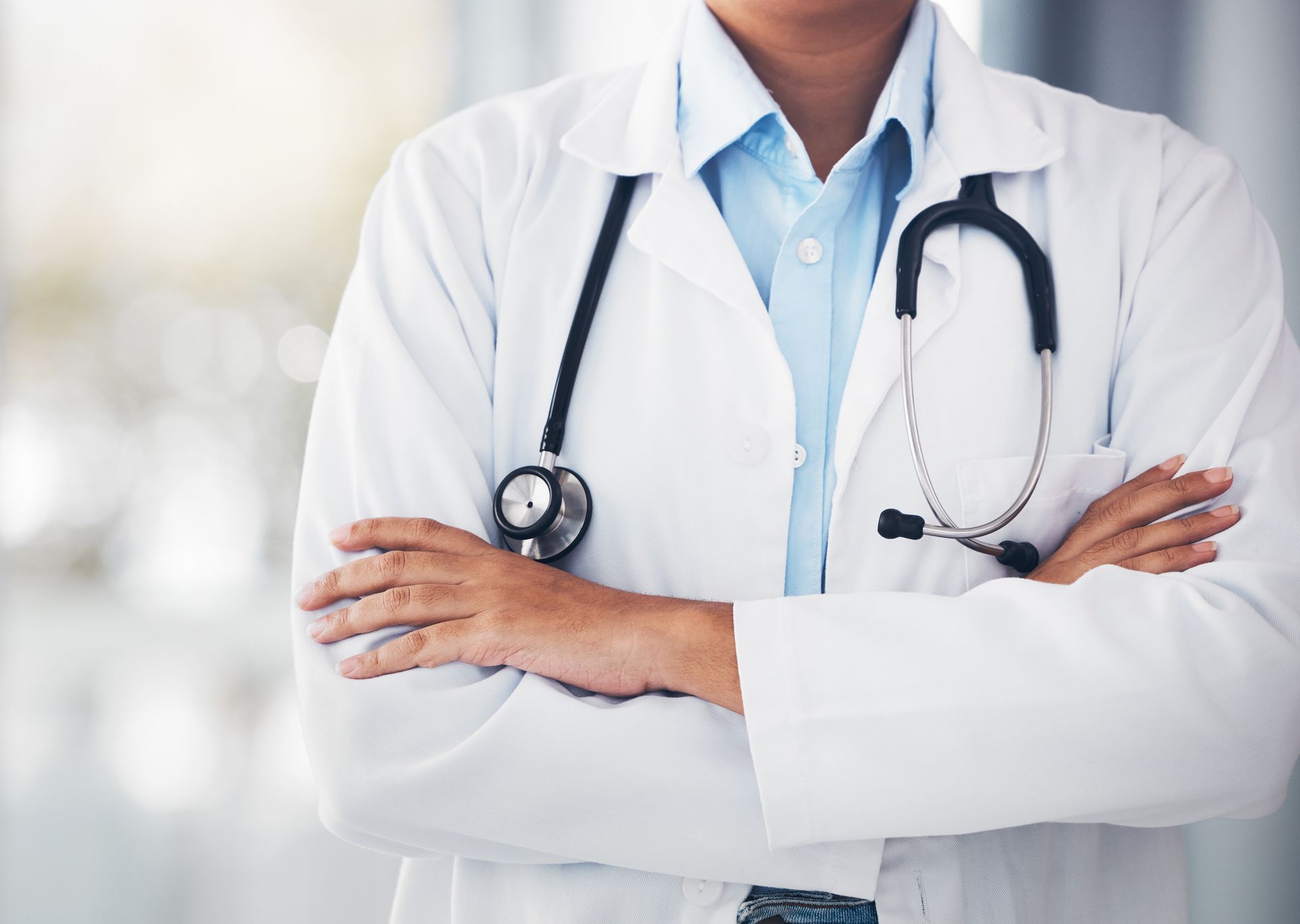 Doctor in white coat with crossed arms, stethoscope around neck.
