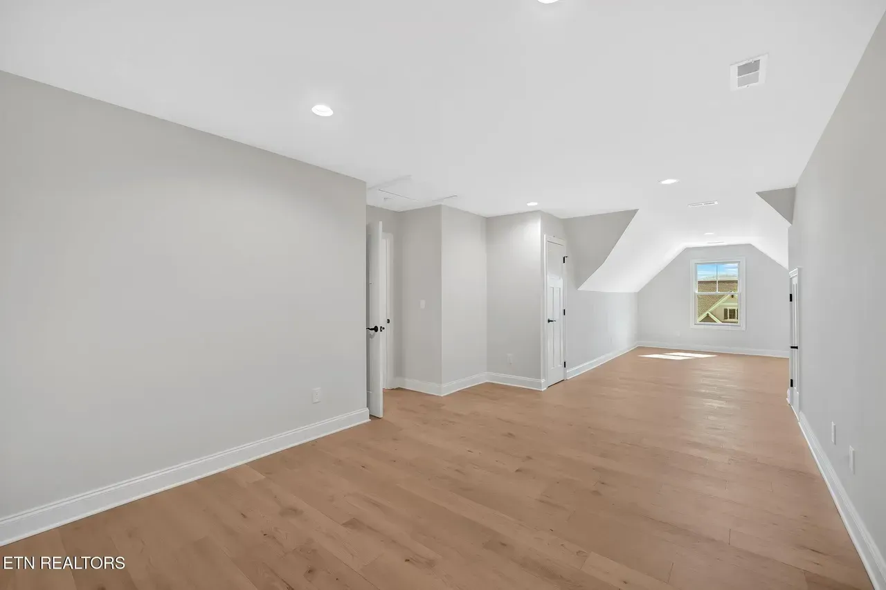 Empty room with light wood floors, white walls, and a small window in the gable.