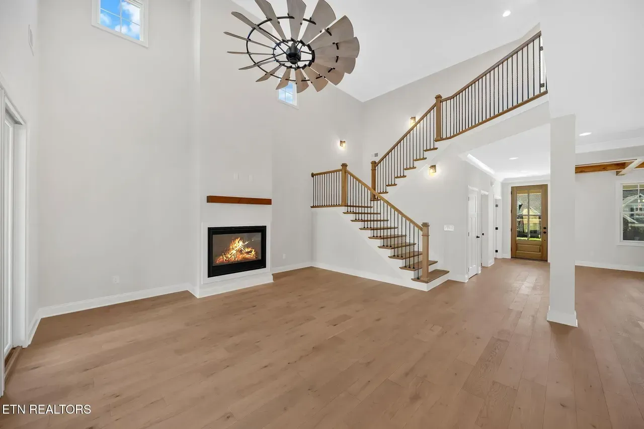 Spacious living room with a fireplace, staircase, and unique ceiling fan.