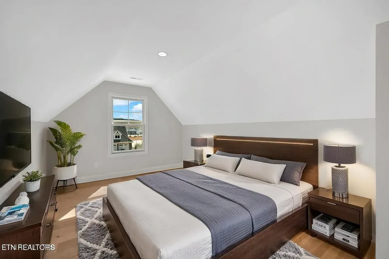 Bedroom with bed, nightstands, and TV. Angled ceiling, window, and rug.
