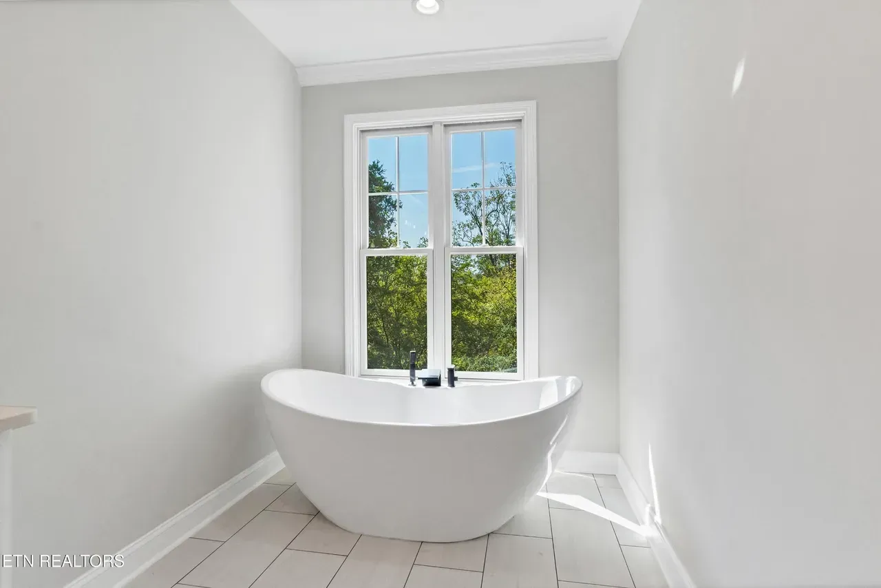 White freestanding bathtub under a window in a modern, light-filled bathroom.