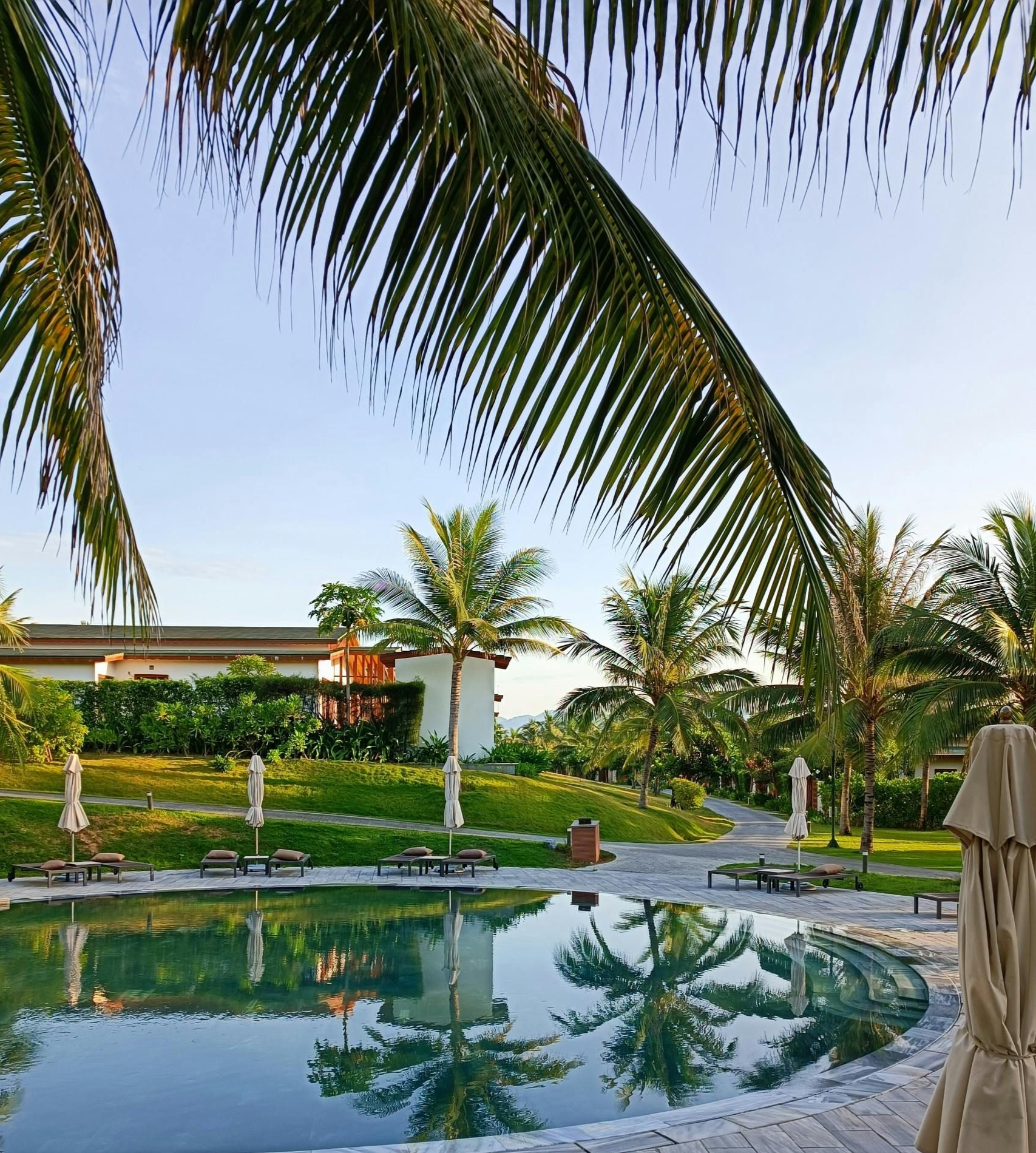 Piscina de resort tropical com palmeiras refletidas na água calma ao pôr do sol