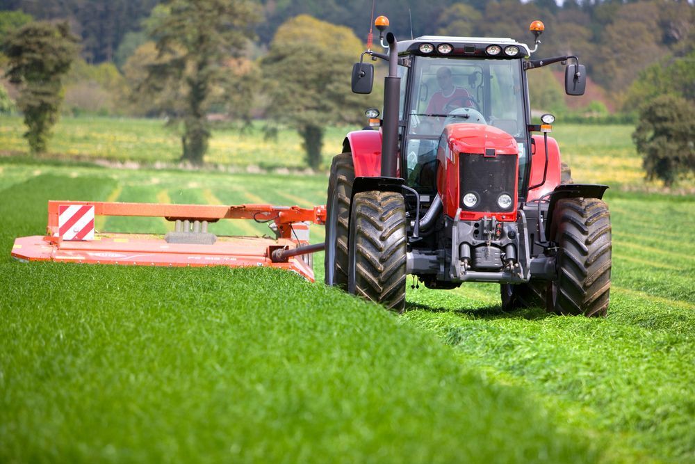 A red tractor is cutting grass in a field. — Nabiac Mower & Tractor Repairs in Nabiac, NSW