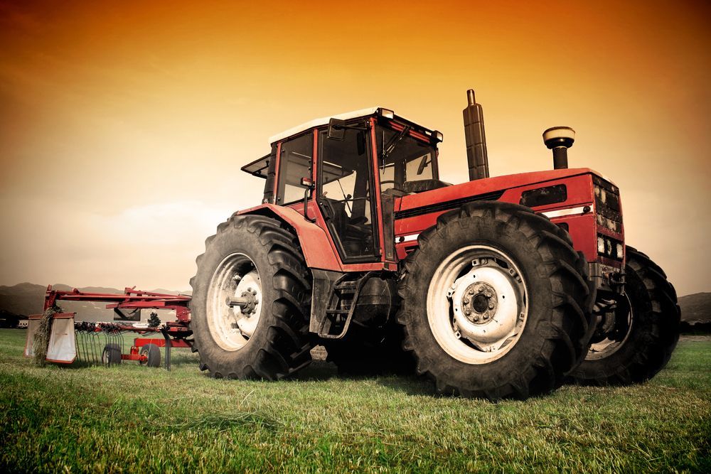 A Man is Working on a Red Tractor With a Screwdriver — Nabiac Mower & Tractor Repairs in Nabiac, NSW