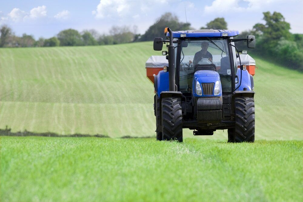 A blue tractor is spraying fertilizer on a lush green field. — Nabiac Mower & Tractor Repairs in Nabiac, NSW