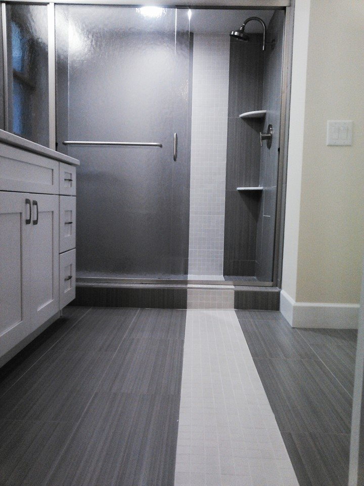 Bathroom with gray and white tiles, glass shower, and white vanity.