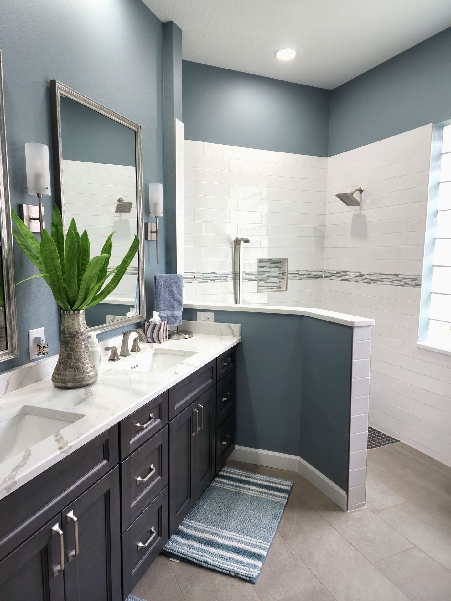 Bathroom with blue walls, white tile shower, dark cabinets, and a large mirror.