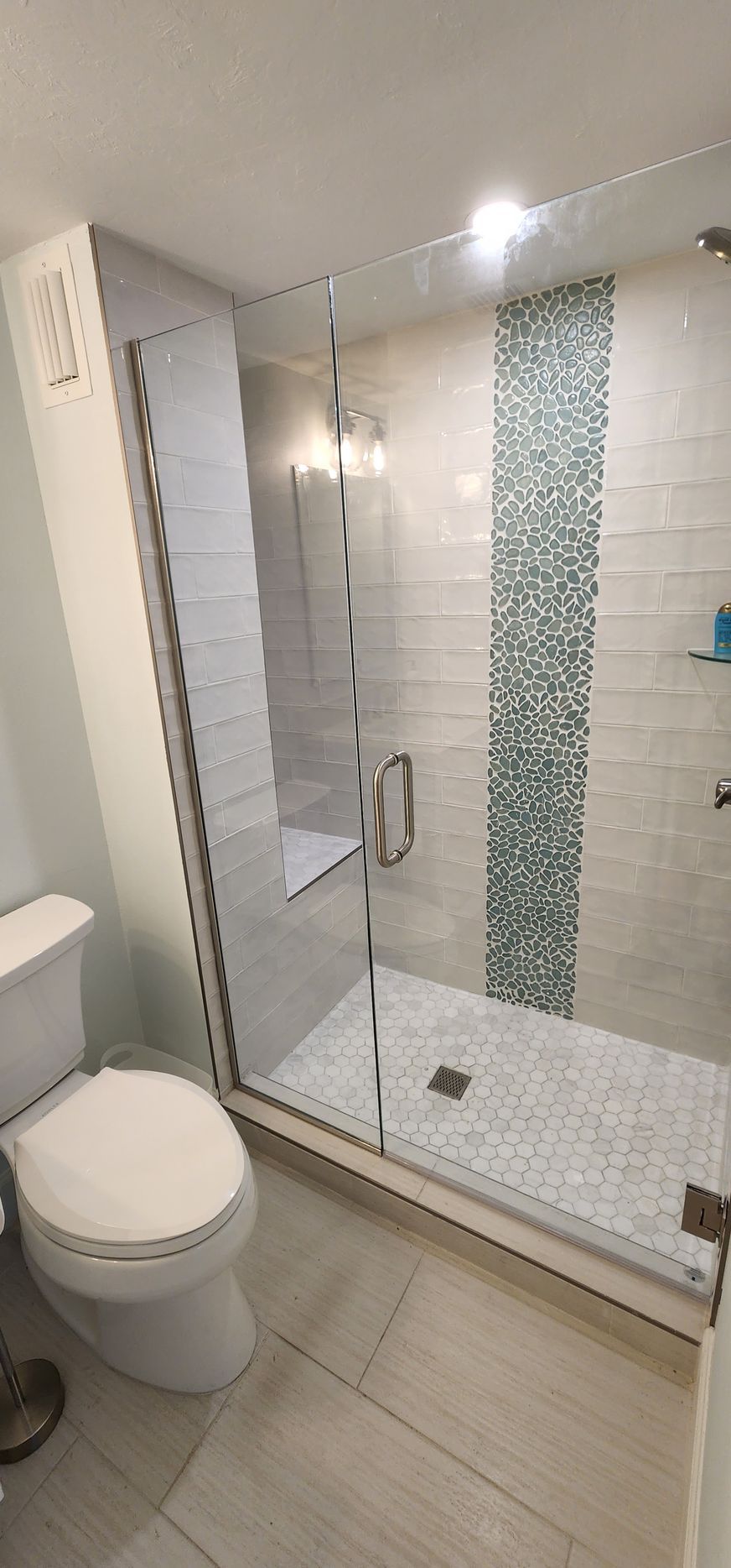 A modern bathroom with a glass shower, white toilet, and light-colored flooring and walls.