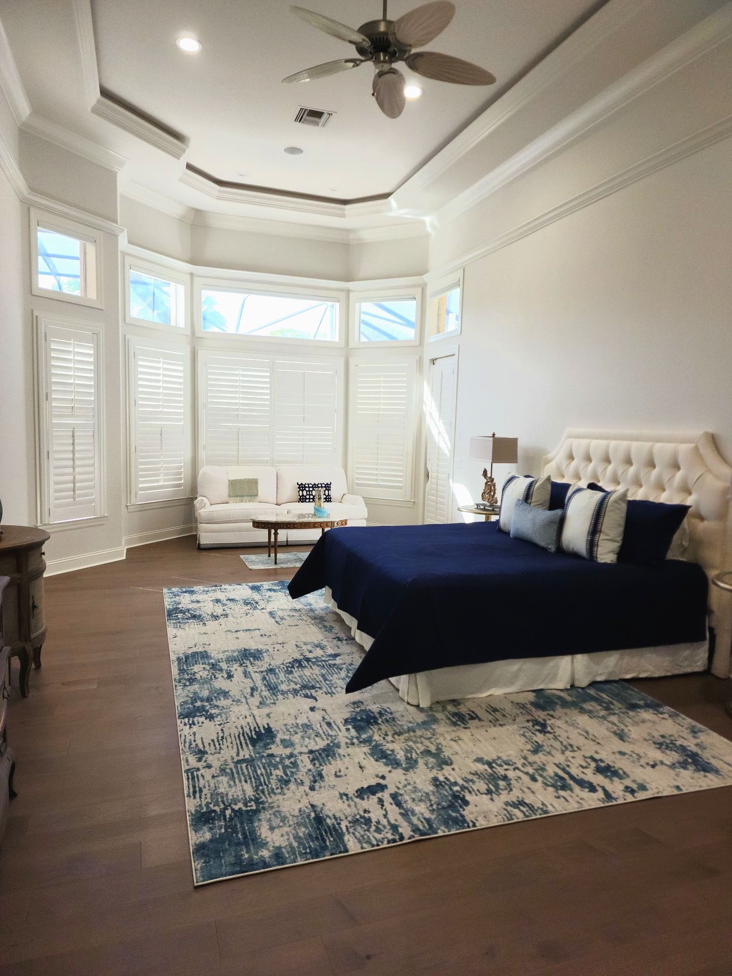 Spacious bedroom with large window, sofa, and a bed with navy blue bedding and blue rug.