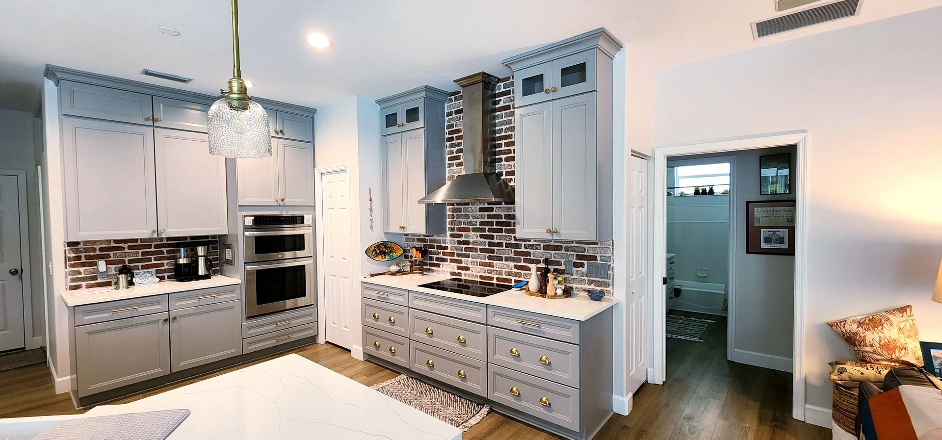 Kitchen with gray cabinets, a range hood, and a view into a bathroom.