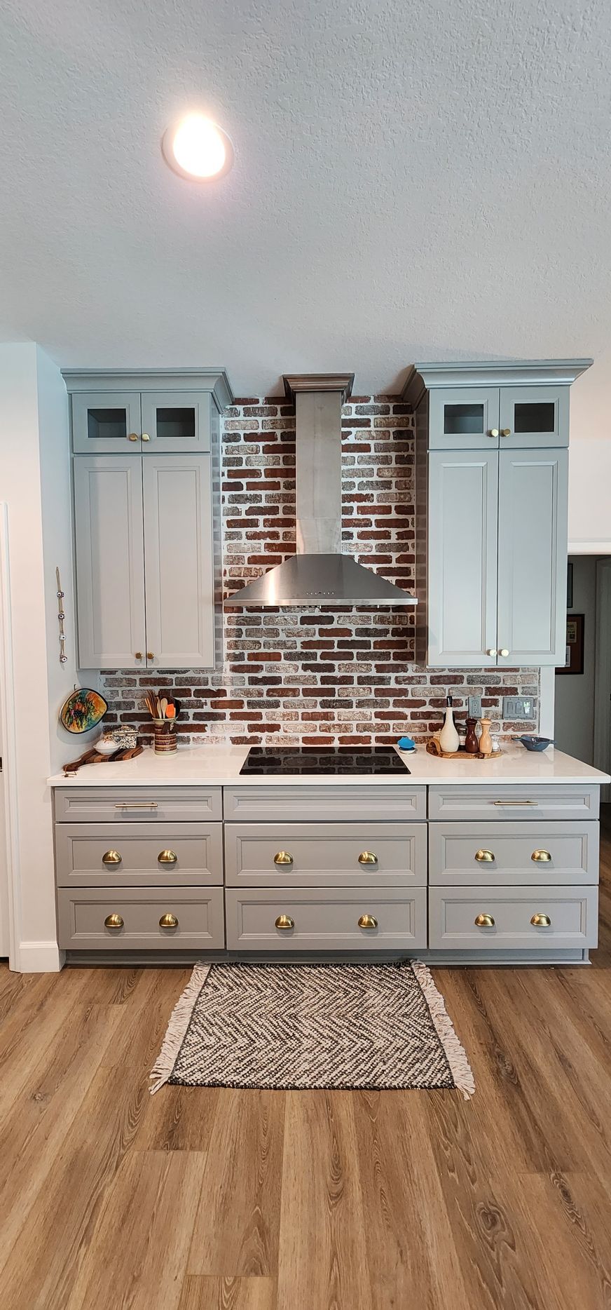 Kitchen with gray cabinets, brick backsplash, and a rug on wood floors.