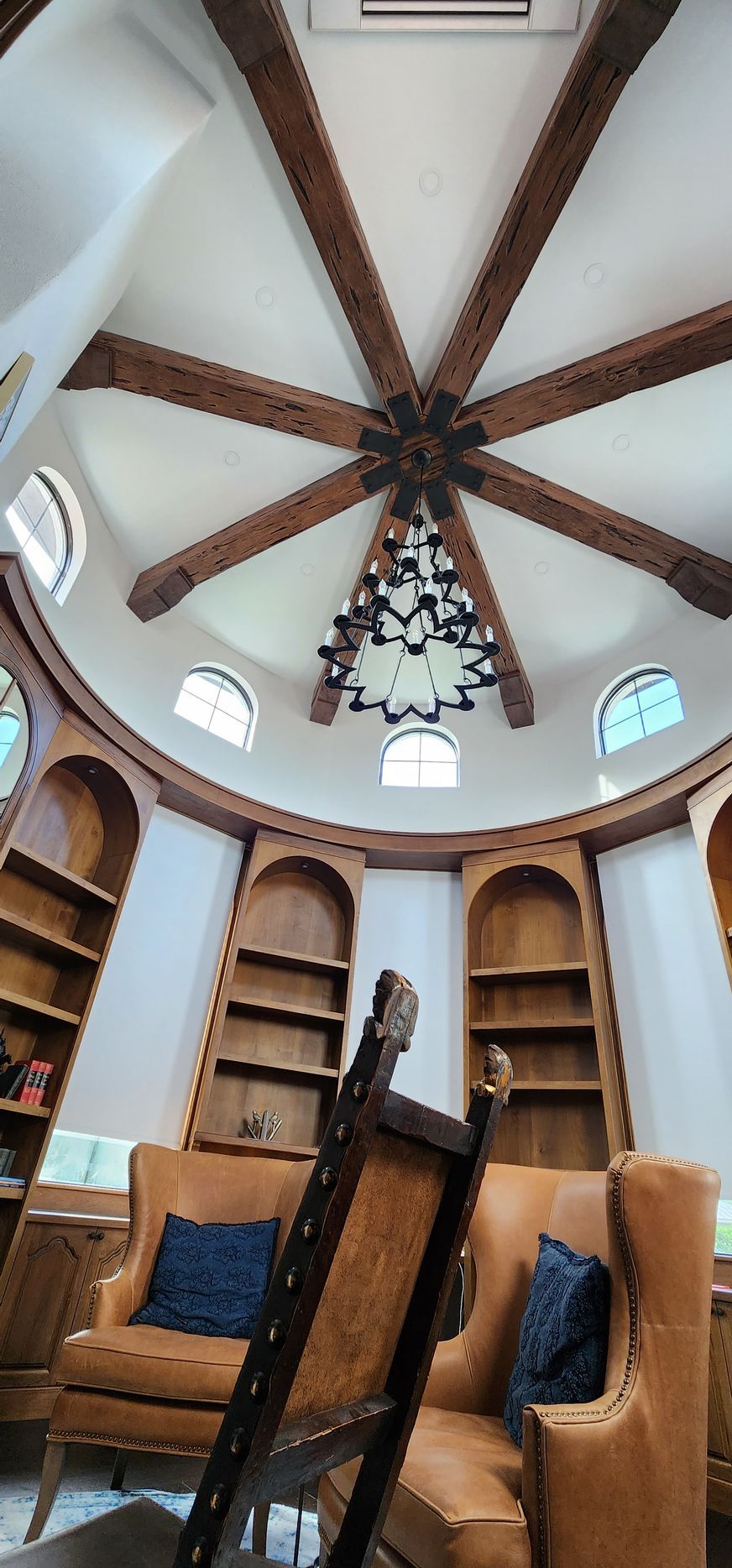 Round room with wooden bookshelves, chairs, and a decorative ceiling with a chandelier.