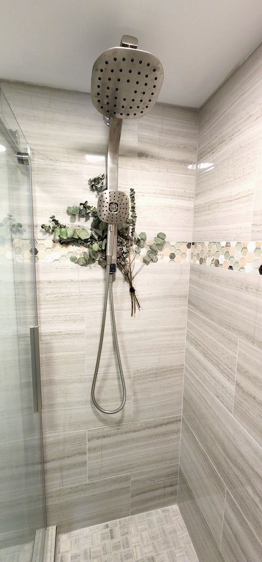 Shower design with light gray tile walls and a silver showerhead. Greenery hangs from the showerhead.