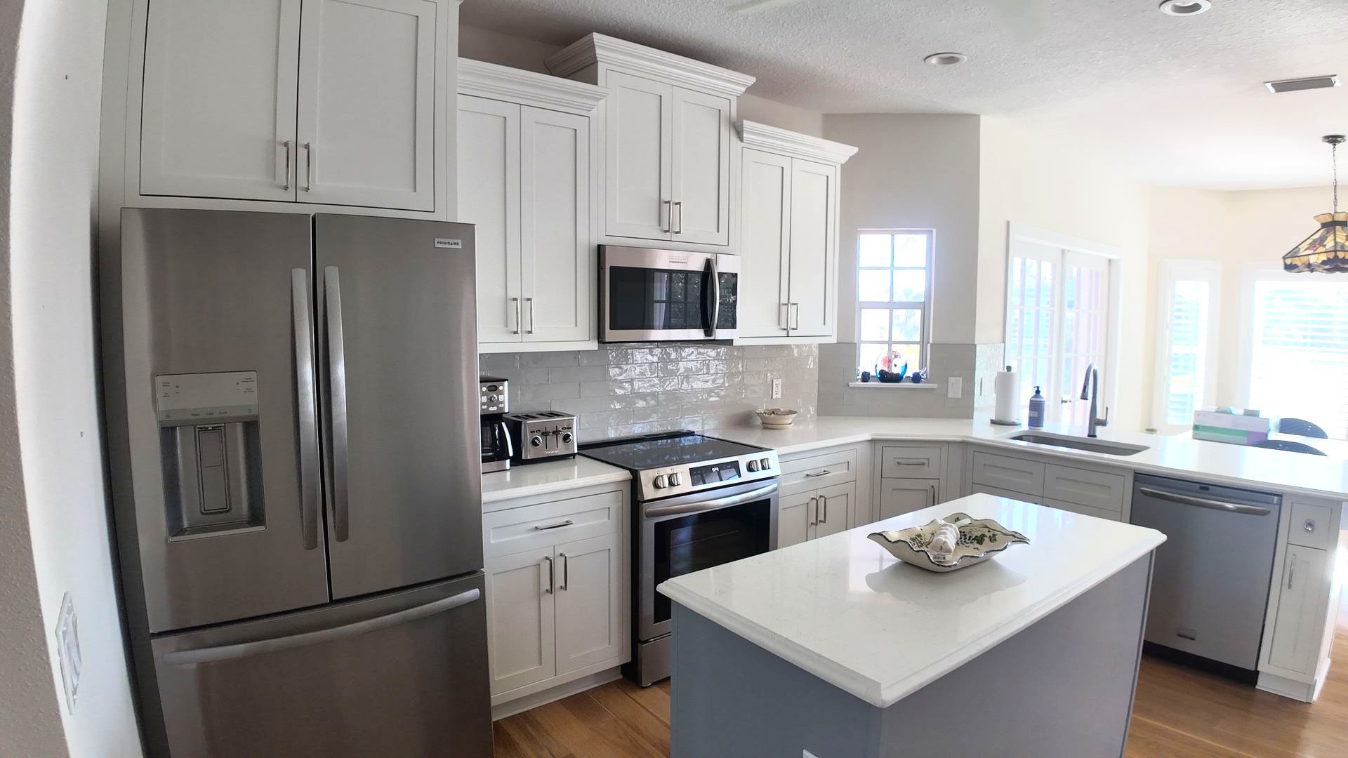 Kitchen with white cabinets, stainless steel appliances, and gray island with a white countertop.