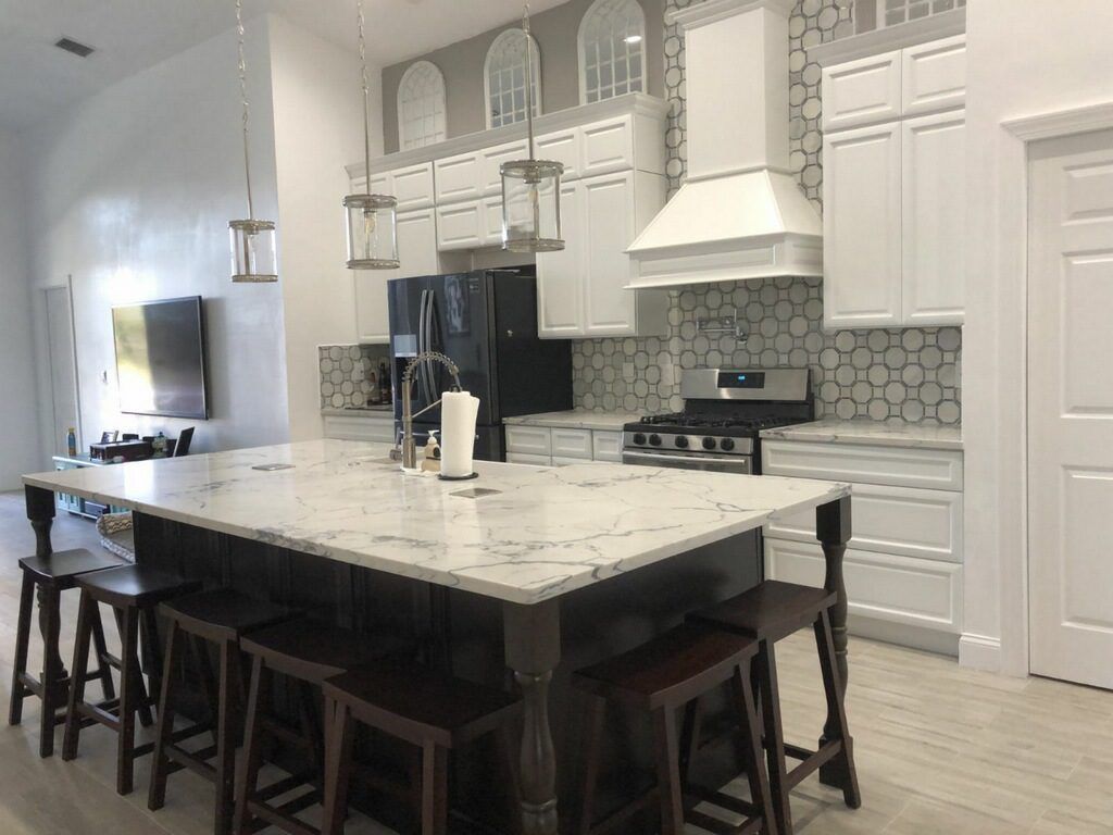 Kitchen with a large island, white cabinets, and a dark fridge; stools sit around the island.