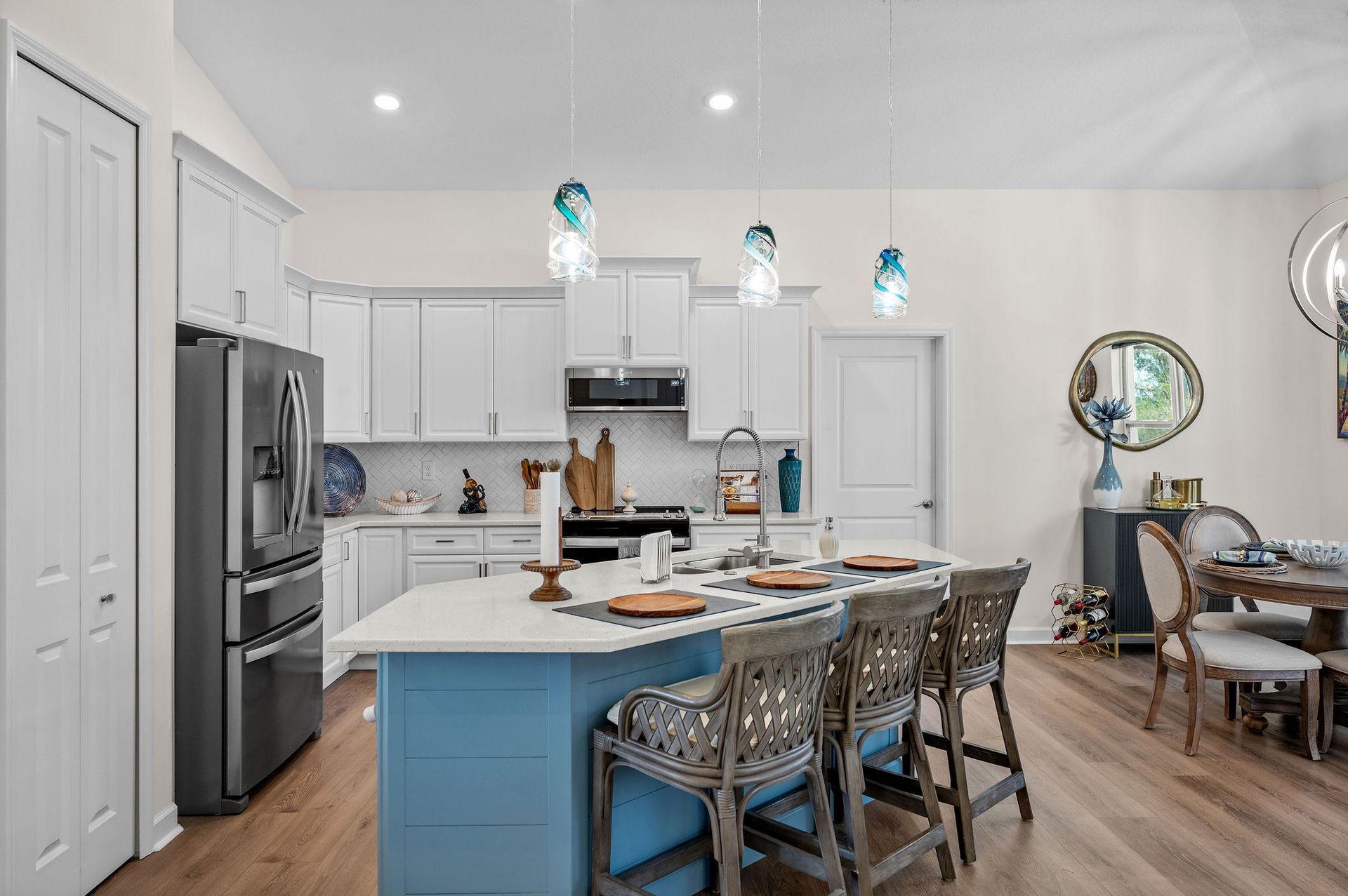 Modern kitchen with a blue island, white cabinets, and wooden flooring.