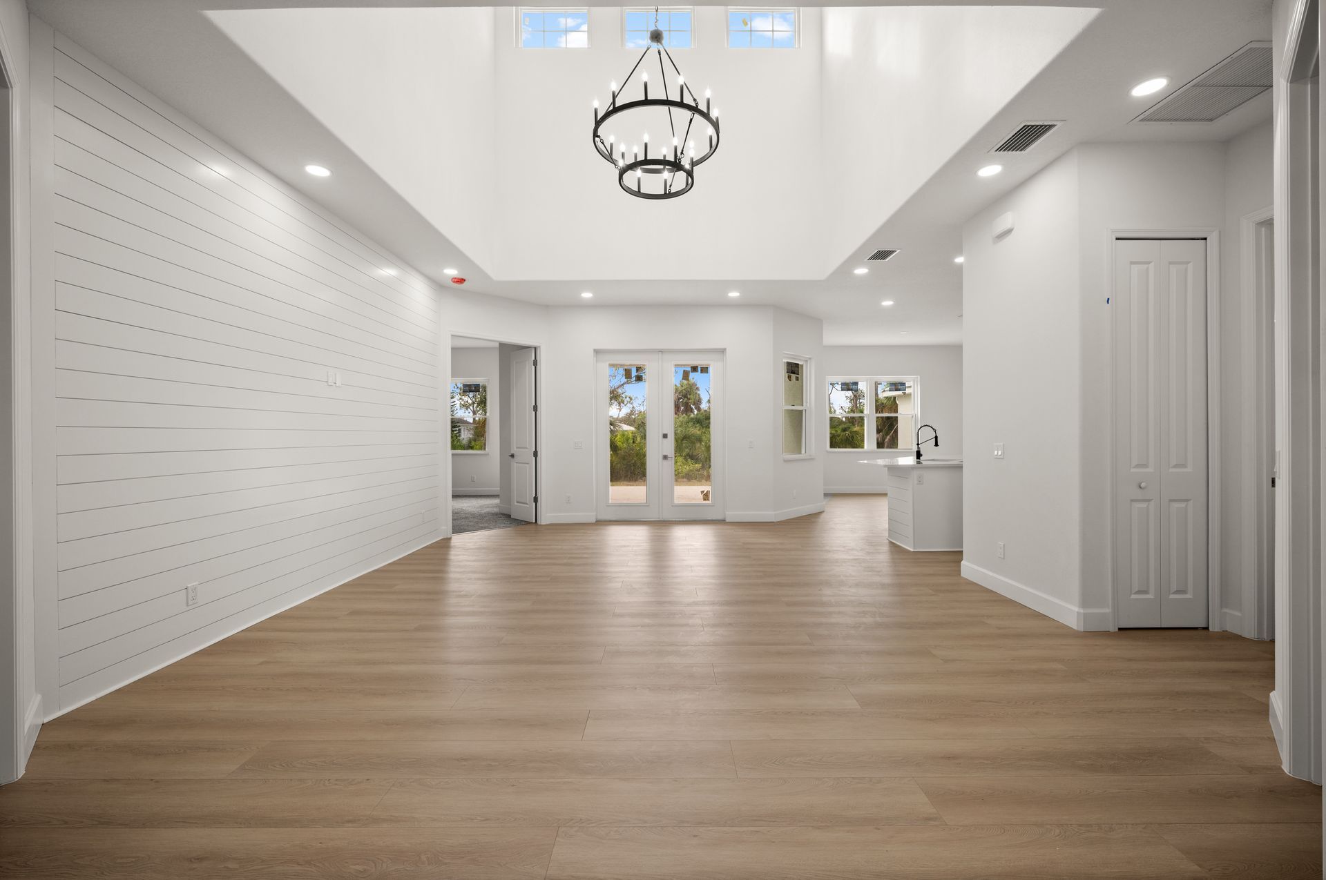 Light-filled interior with hardwood floors. Features a high ceiling, chandelier, and doors to the outside.