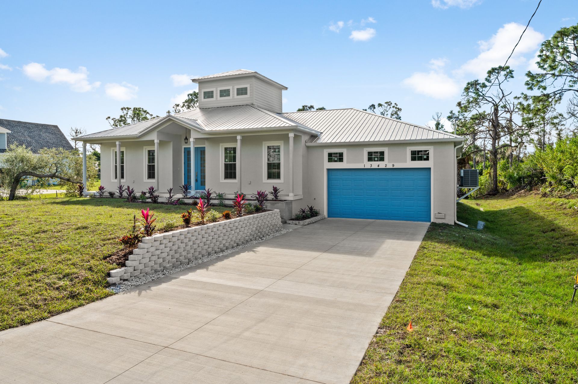 Modern gray house with blue door and garage, driveway, and landscaped yard.