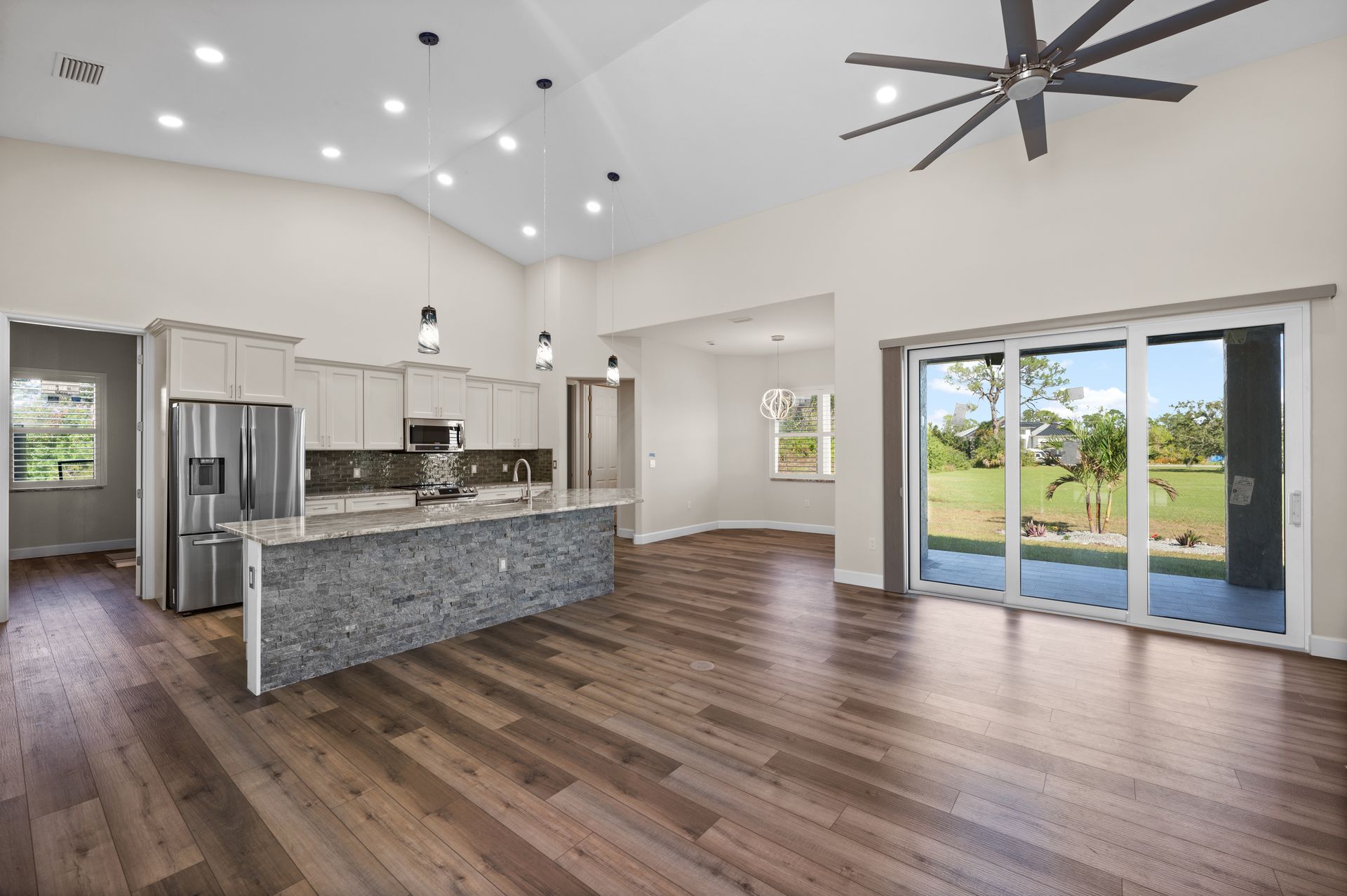 Open-concept kitchen and living room with wood floors, granite countertops, and a view of greenery.