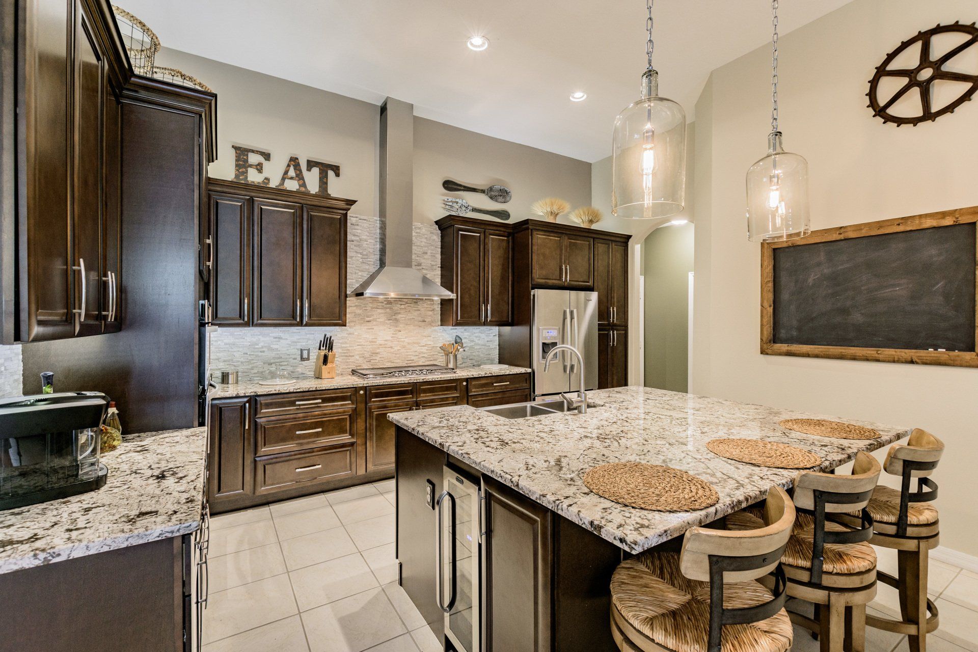 Kitchen with dark cabinets, granite counters, island with stools, and decorative accents.