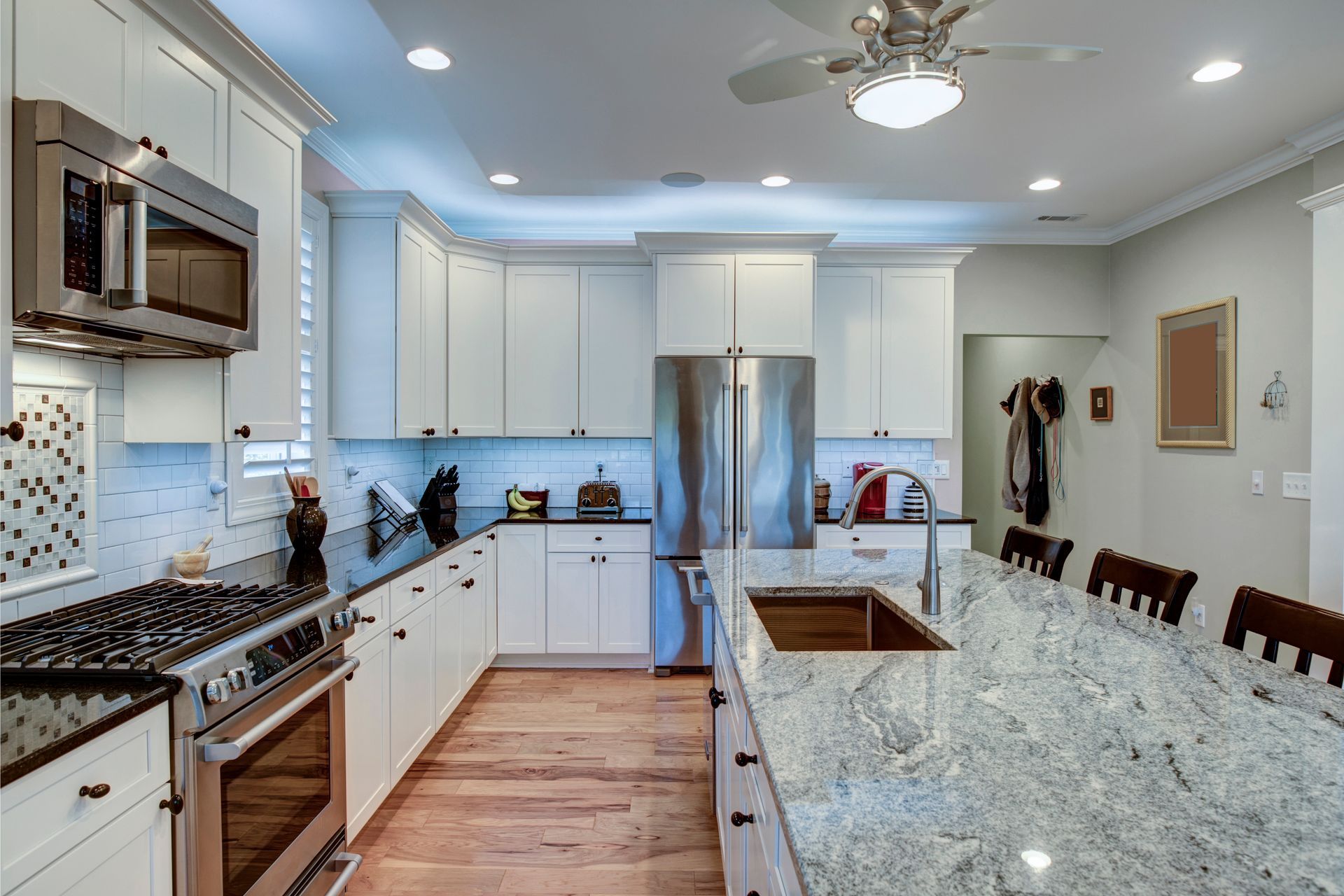 Modern kitchen with white cabinets, stainless steel appliances, granite countertops, and an island with seating.