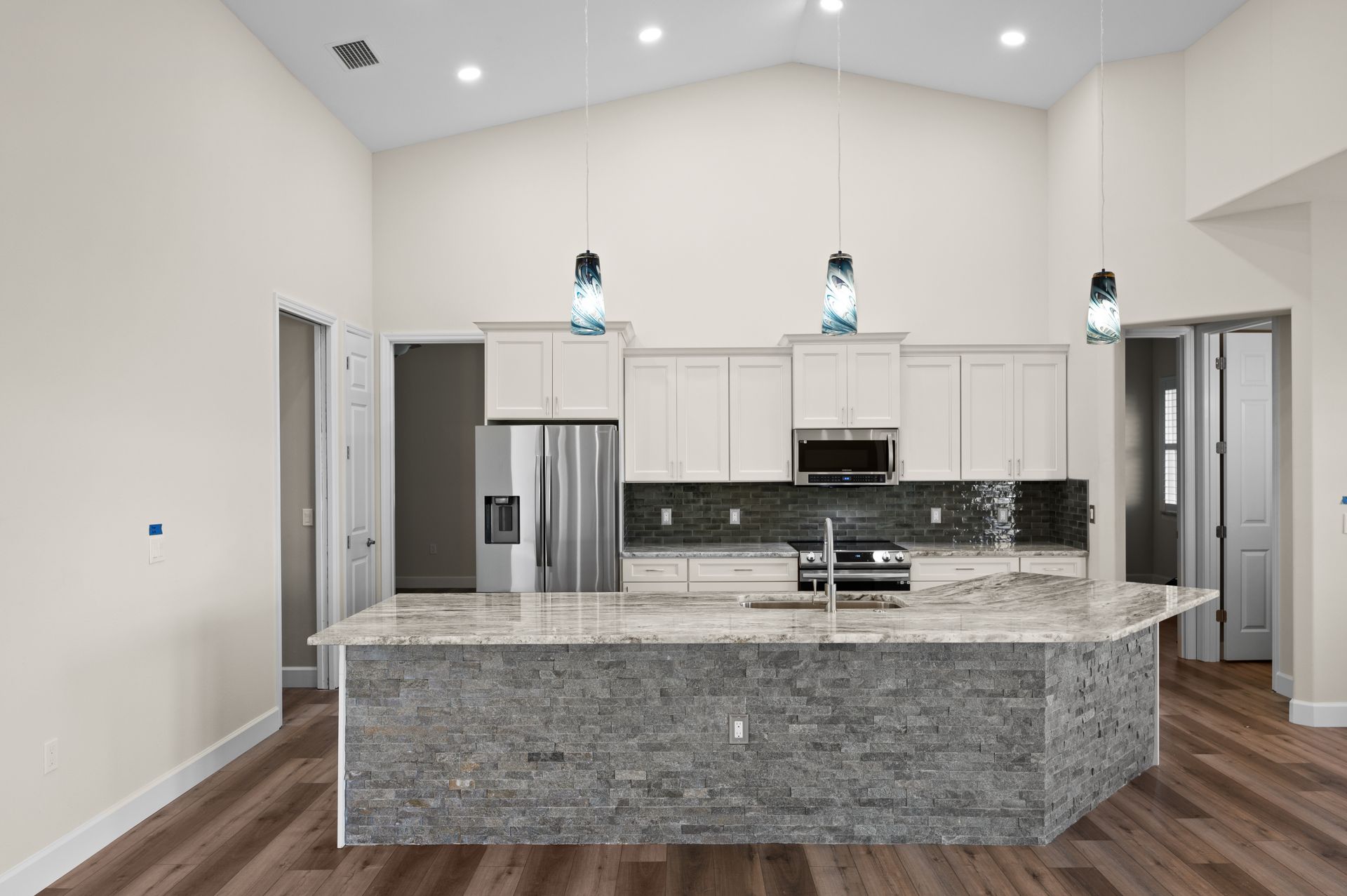 Kitchen with a large island, stainless steel appliances, and pendant lights.