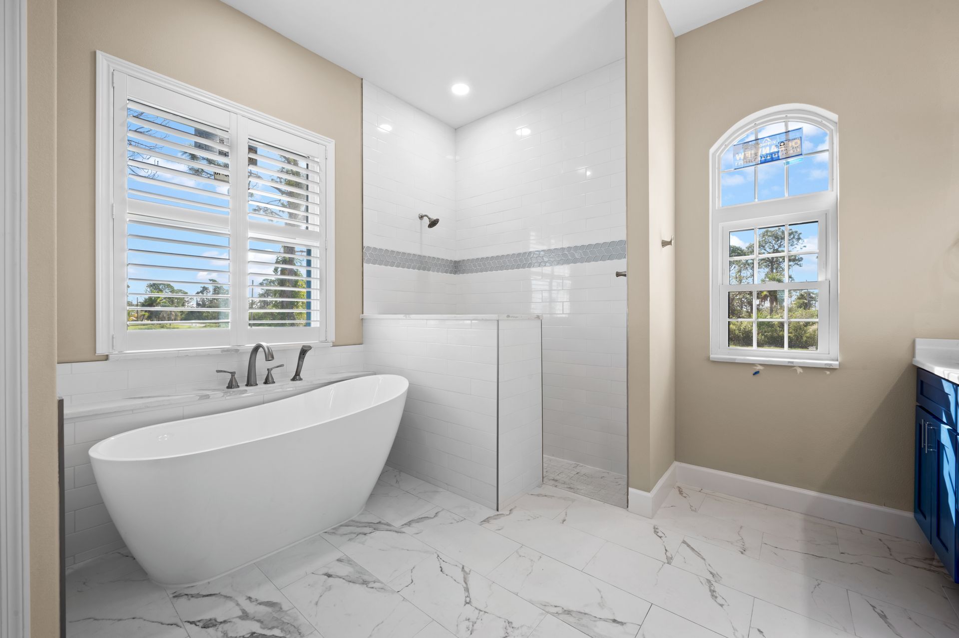 Elegant bathroom with a white soaking tub, shower, and marble floors, bathed in natural light.