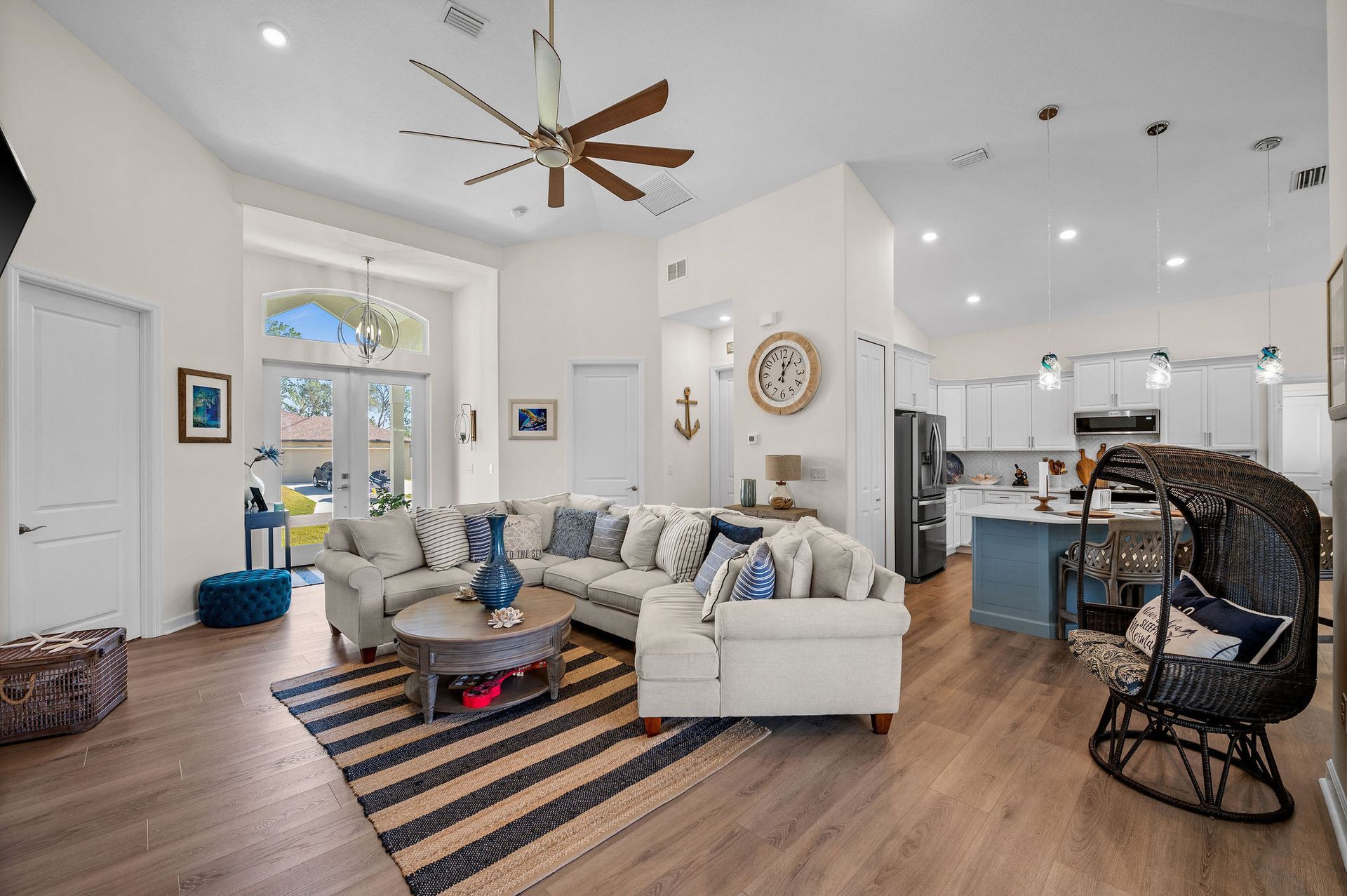 Coastal-themed living room with white walls, sectional sofa, striped rug, and open kitchen.