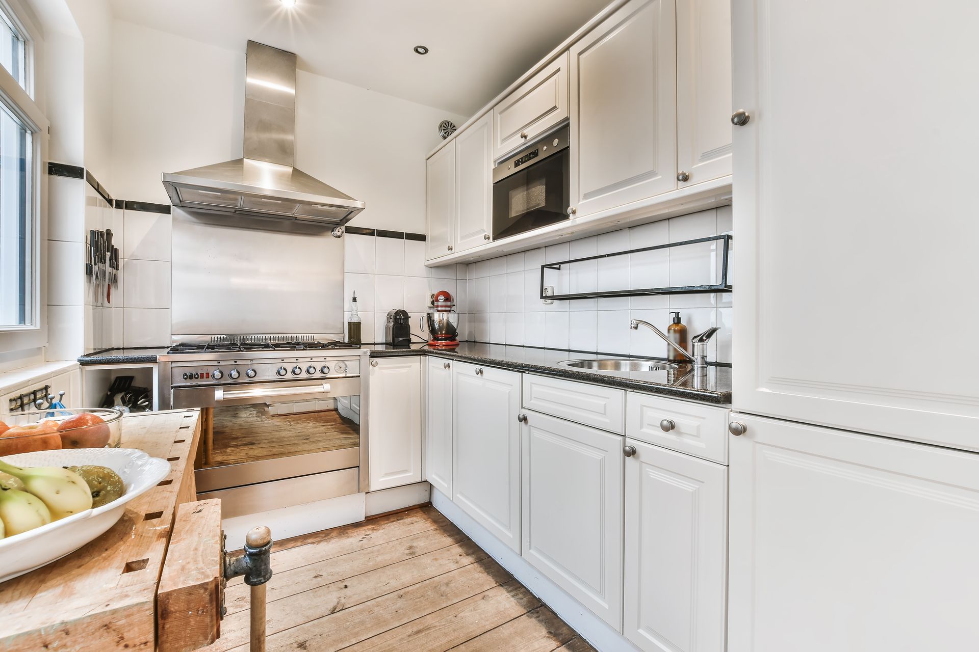 White kitchen with stainless steel range hood, cabinets, and black countertops.